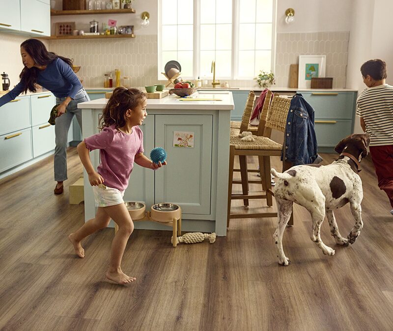 Family and dog running around the kitchen while Mom takes food out of the oven on dark, waterproof, and scratchproof luxury vinyl flooring.